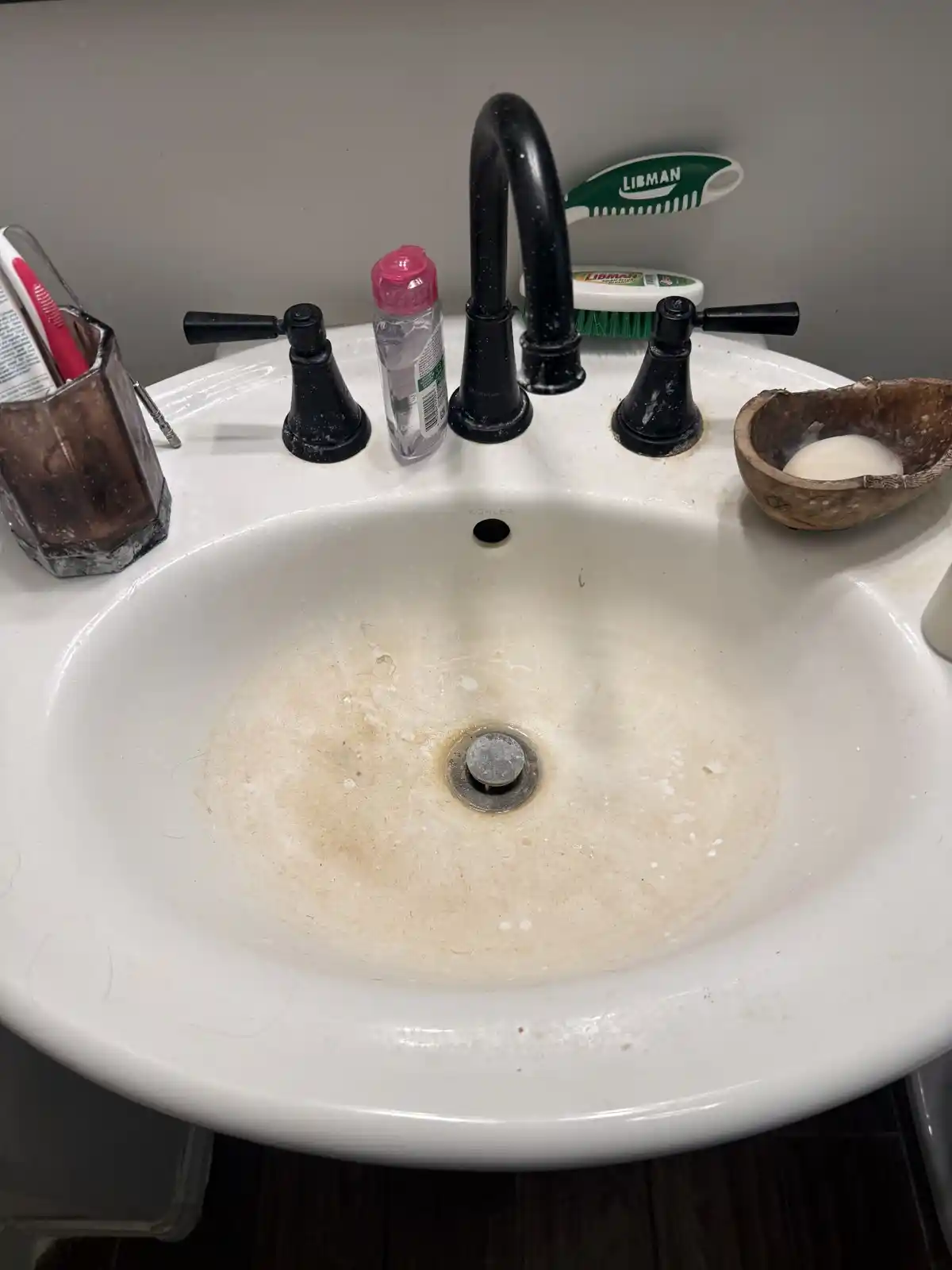 A bathroom sink basin with brown stains around the drain, before cleaning