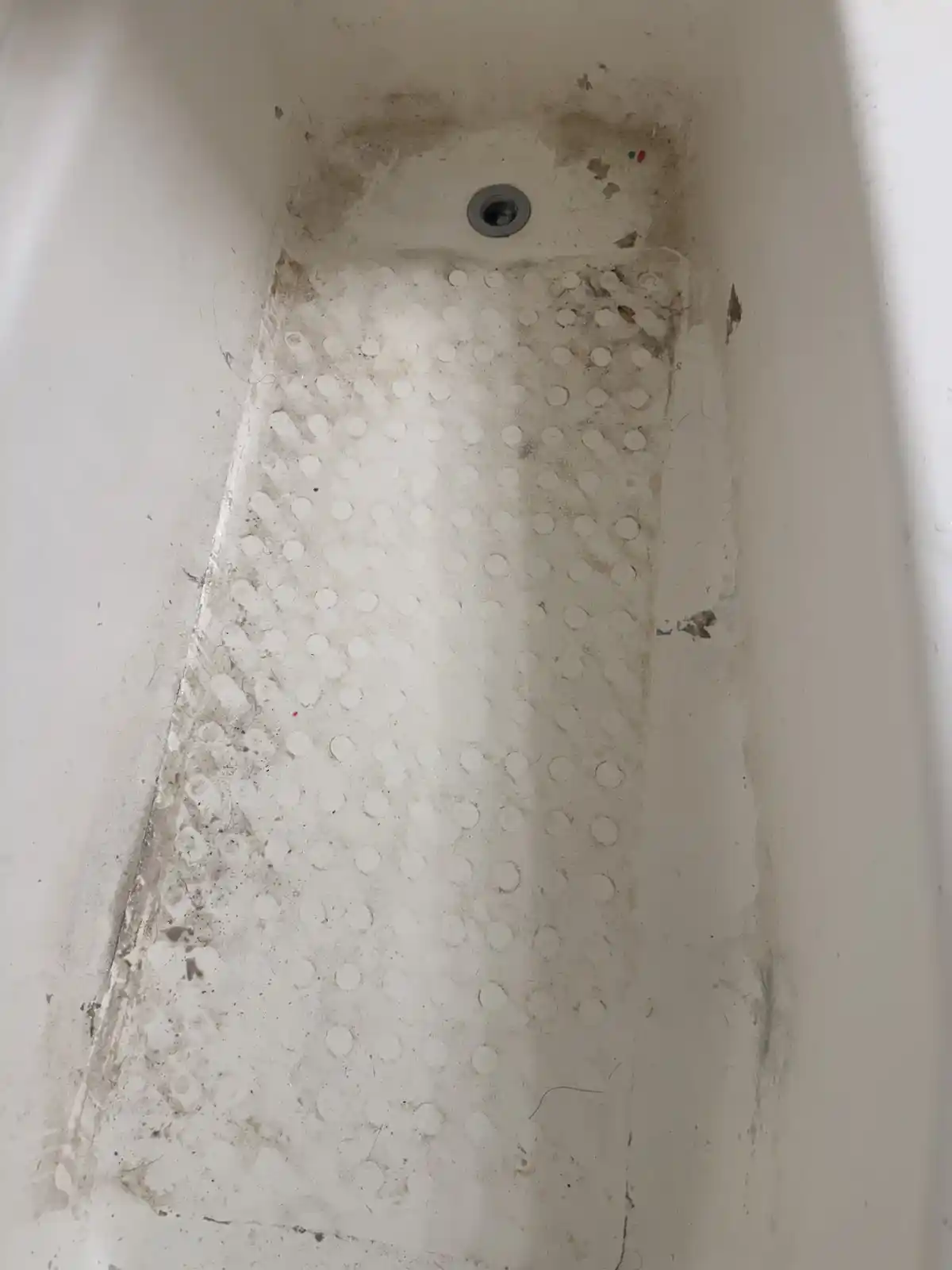 A bathtub floor streaked with soap scum and dirt, before cleaning