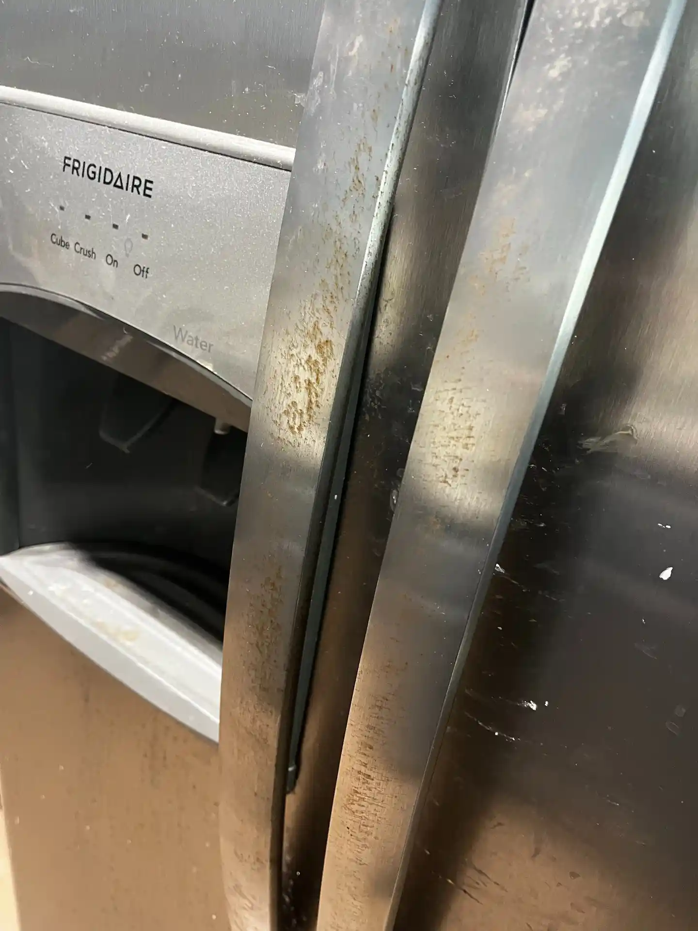 Stainless steel refrigerator doors covered in fingerprints and dried spills, before cleaning