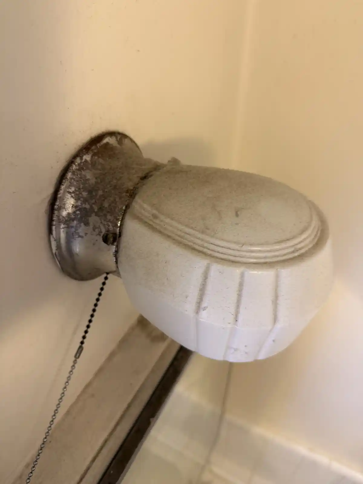 A bathroom wall light with a dusty, grimy glass shade, before cleaning
