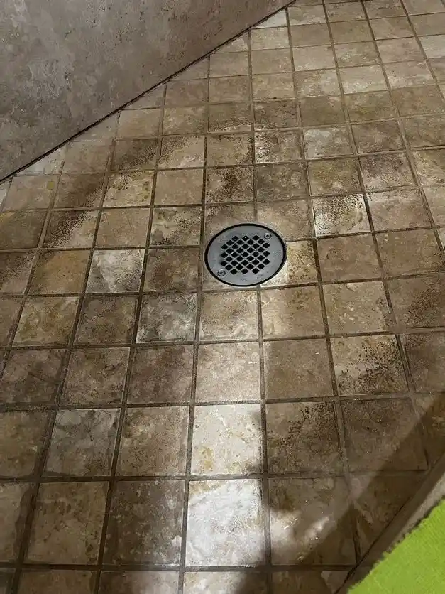 A tiled shower floor dark with grime in the grout, before cleaning