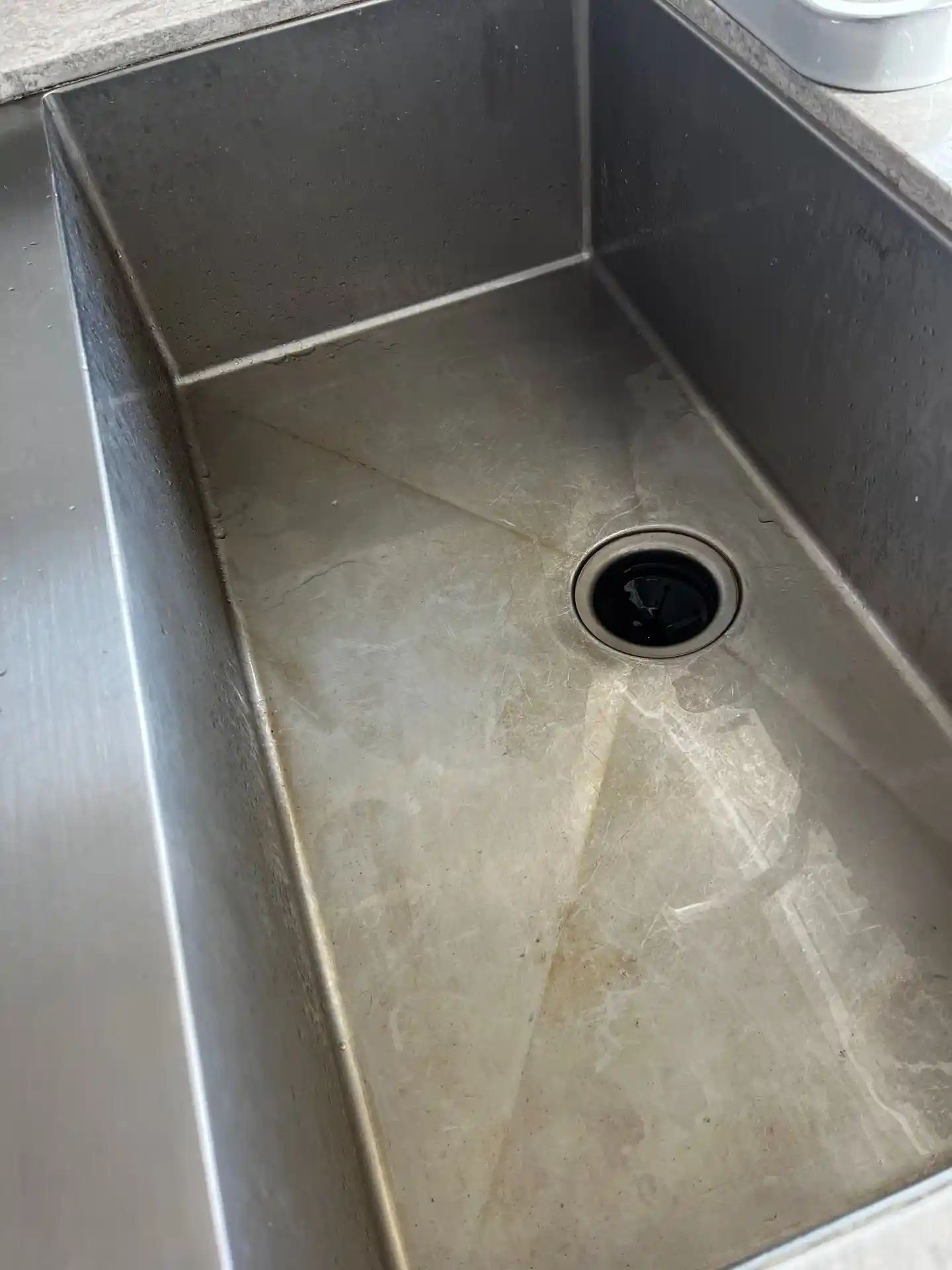 A stainless steel kitchen sink with water stains and residue, before cleaning