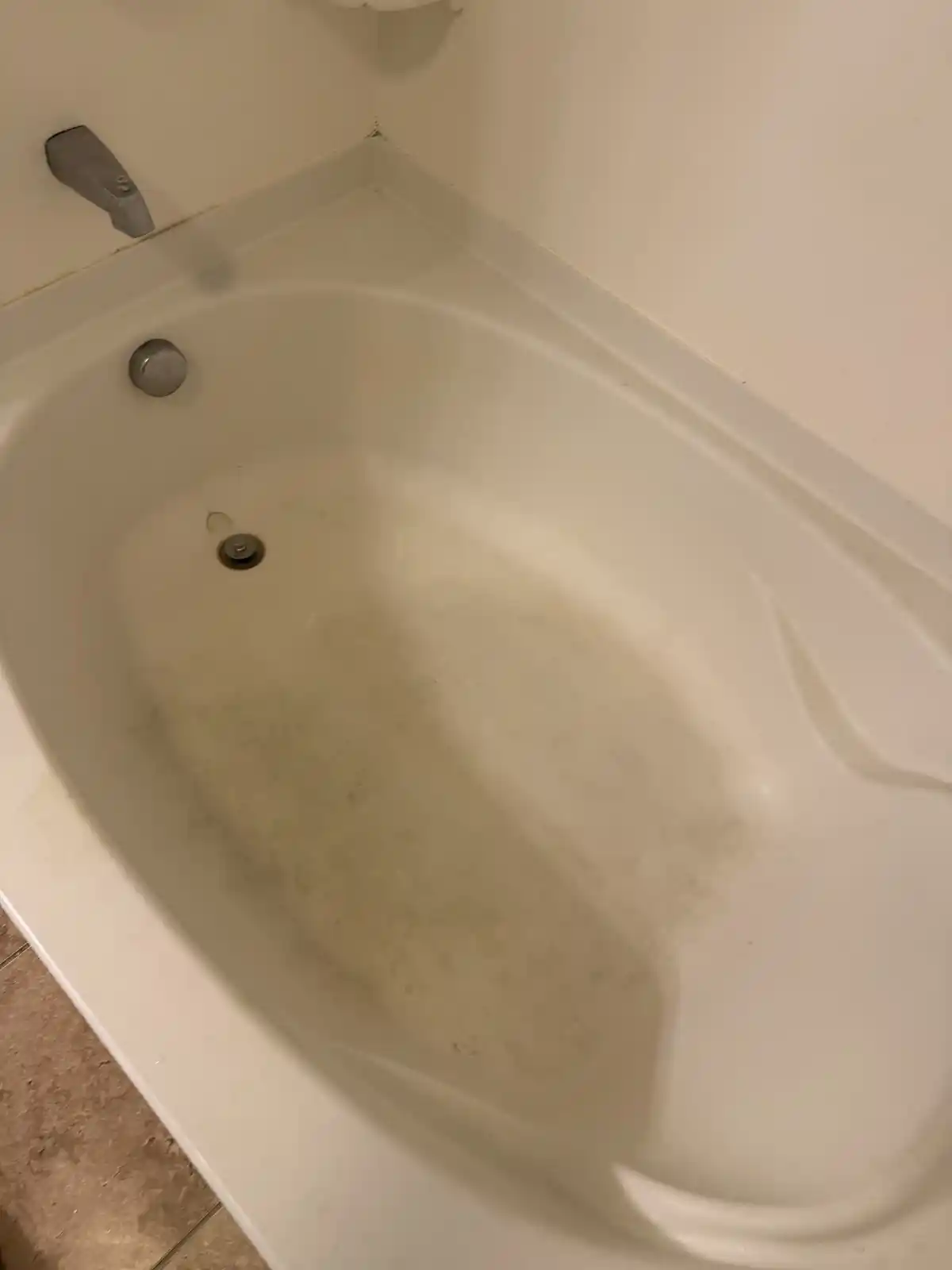 A soaking tub with a dingy stained floor, before cleaning