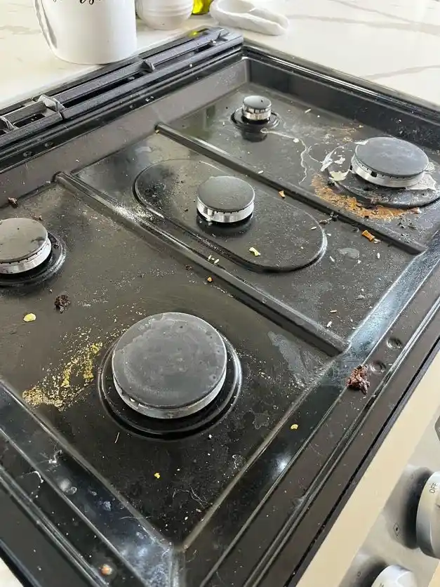 A gas stovetop with burnt-on food and grease around the burners, before cleaning