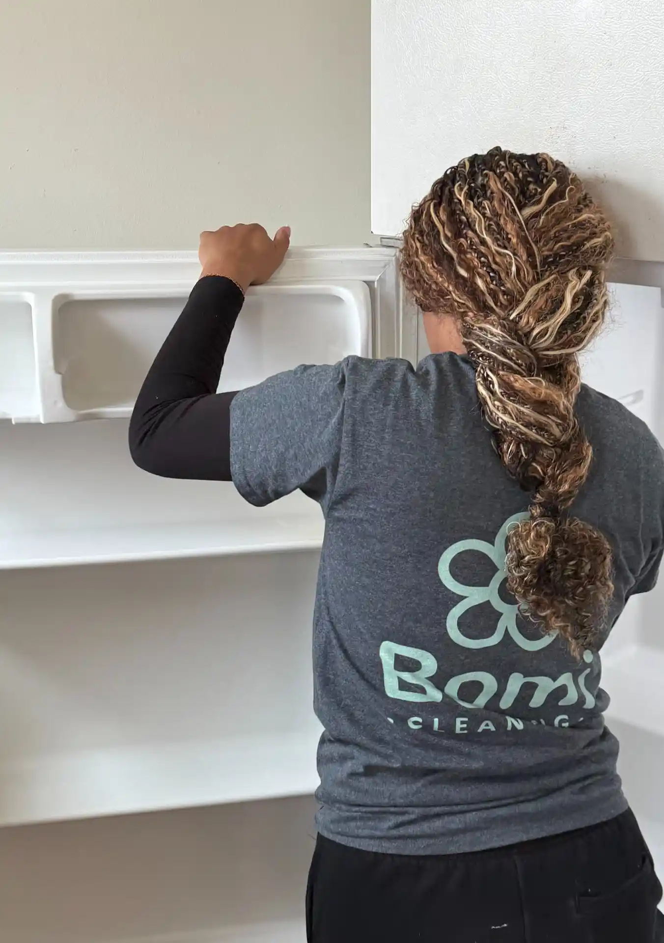 A Bomi Cleaning team member in a Bomi shirt cleaning the inside of a refrigerator